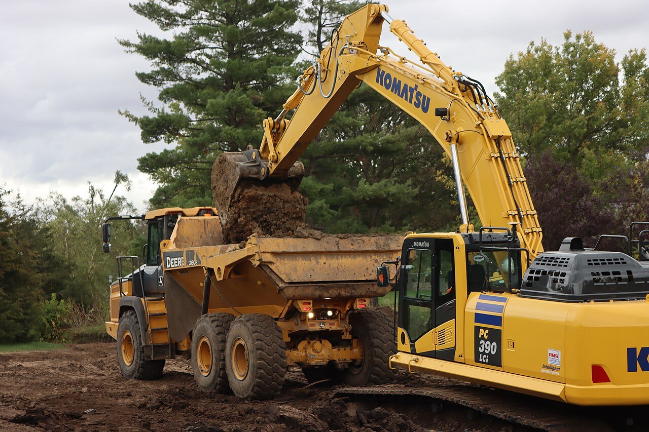 Excavator emptying its bucket into an articulated dump truck on an earthworks site
