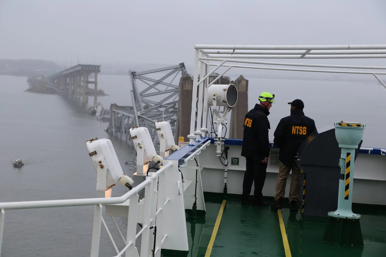 Two NTSB investigators on the deck of the Dali looking at the collapsed Key Bridge truss in fog
