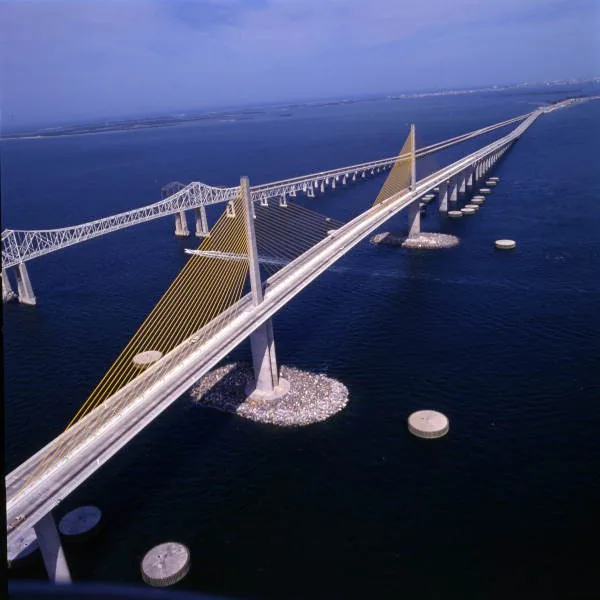 Aerial photo of the cable-stayed Sunshine Skyway Bridge with round concrete dolphins and a rock island around its main pier