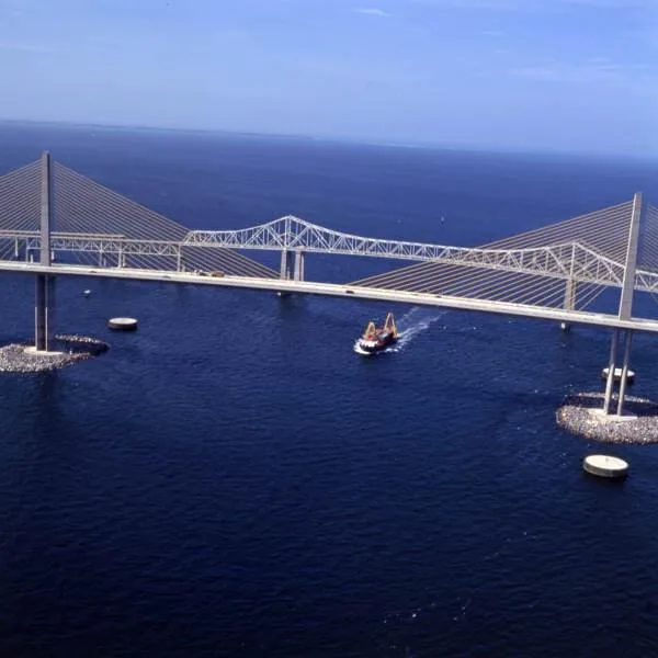 Aerial photo of a ship passing under the Sunshine Skyway main span between rock islands at the pylons, with round concrete dolphins nearby
