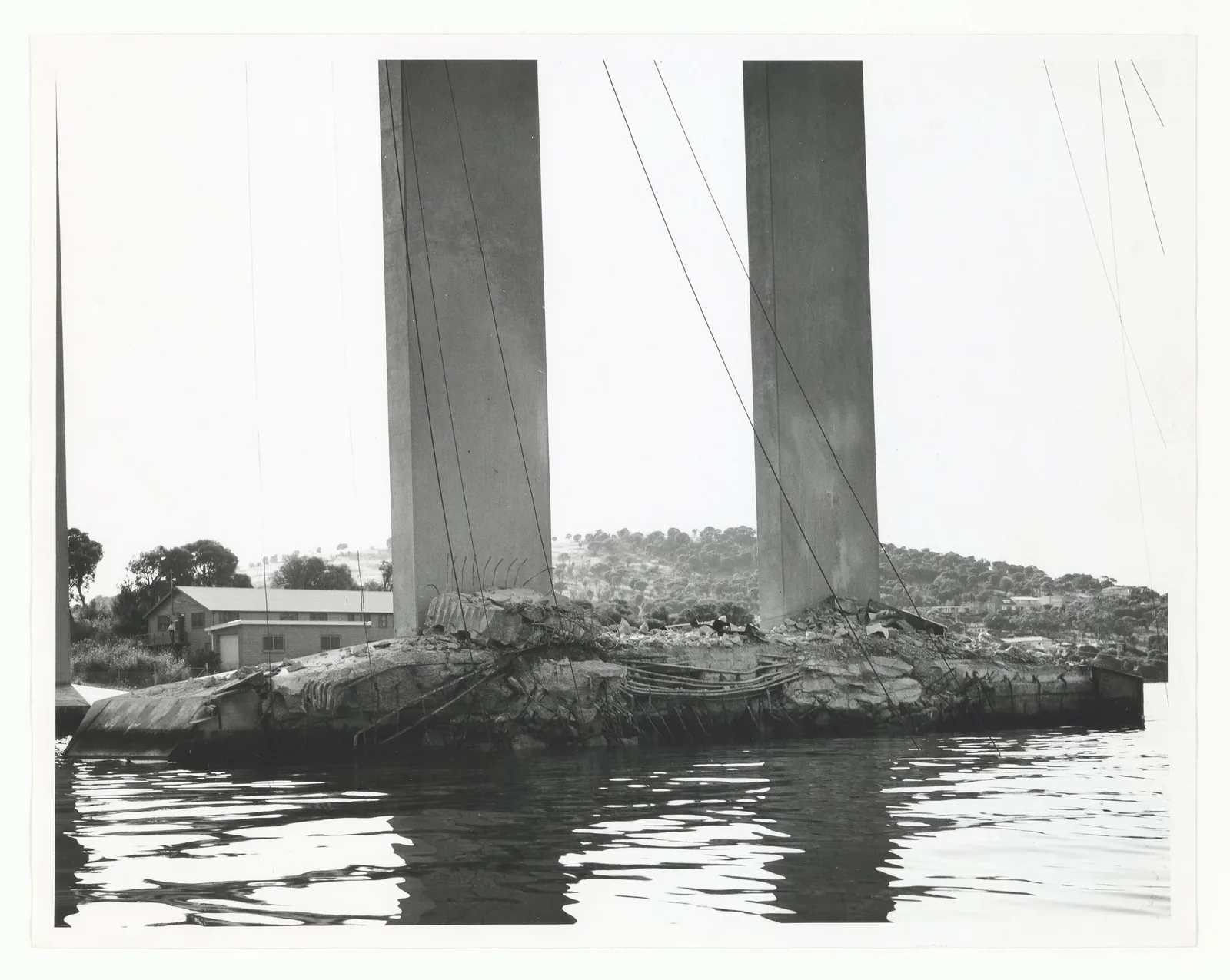 Black and white photo of two broken concrete pier columns of the Tasman Bridge standing in the Derwent River in 1975